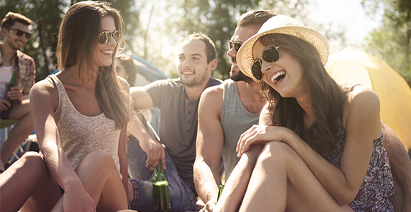 Ein Gruppe junger Leute sitzt in kurzen Klamotten und mit Sonnenbrillen auf einer Wiese zusammen